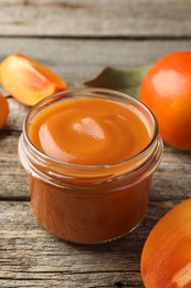 Delicious persimmon jam in glass jar and fresh fruits on wooden table, closeup