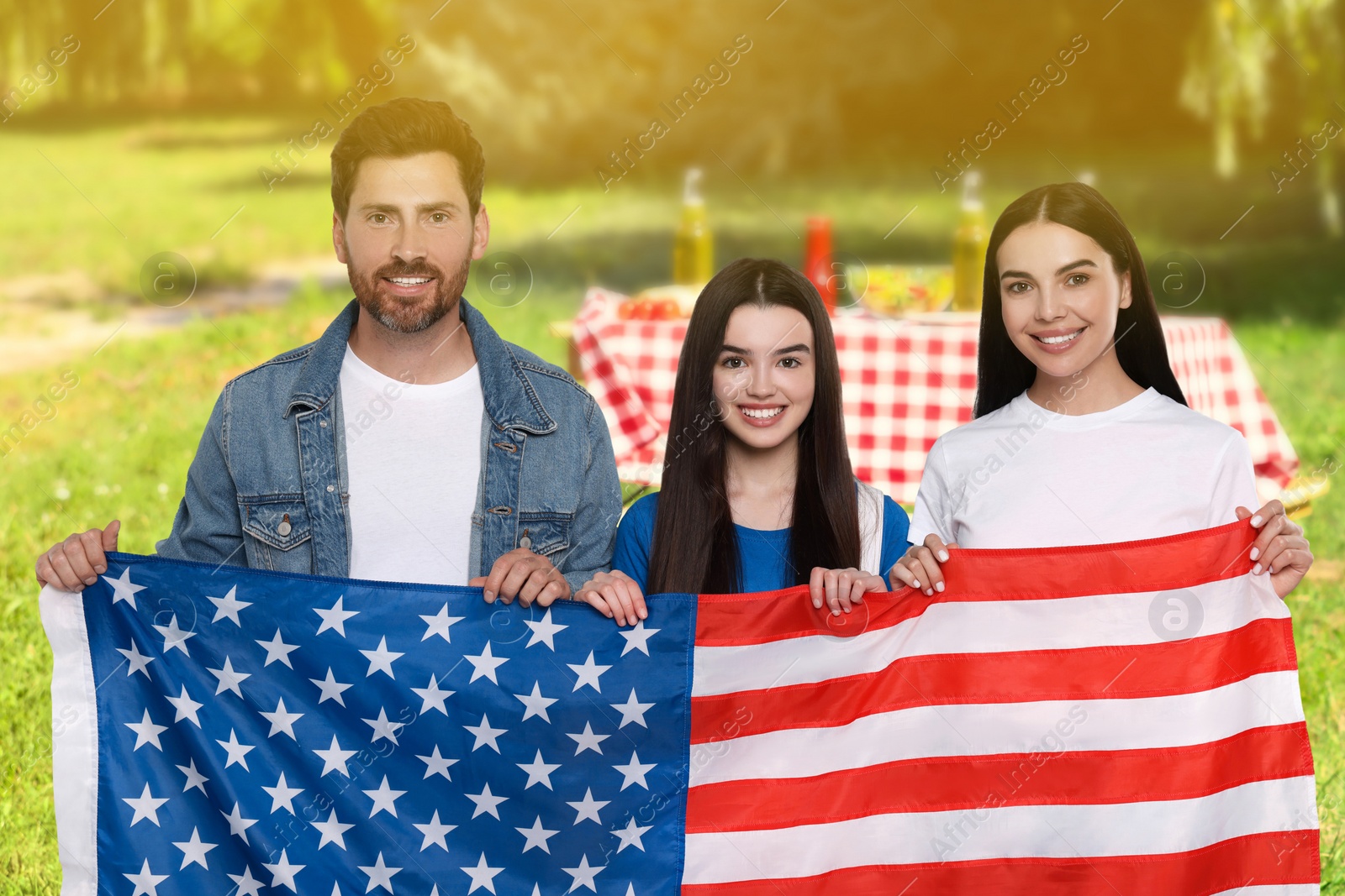 Image of 4th of July - Independence day of America. Happy family with national flag of United States having picnic in park