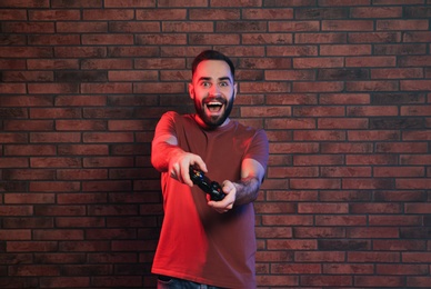 Emotional man playing video games with controller near brick wall