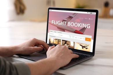 Man using laptop to book flight at white table, closeup