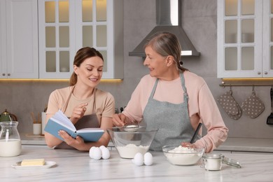 Happy women cooking by recipe book in kitchen
