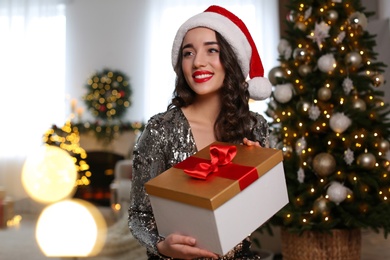 Photo of Beautiful young woman in Santa hat with Christmas gift at home