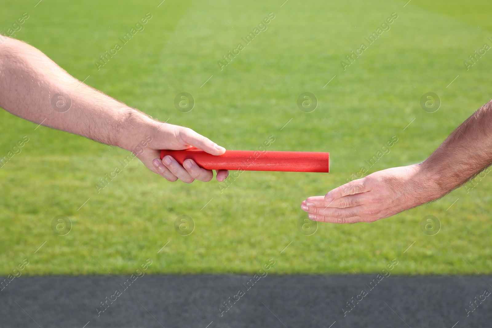 Photo of Man passing baton to his partner at stadium, closeup