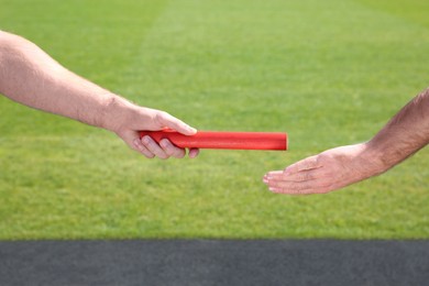 Man passing baton to his partner at stadium, closeup