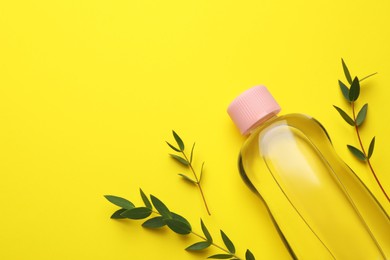 Photo of Bottle of baby oil and green leaves on yellow background, flat lay. Space for text