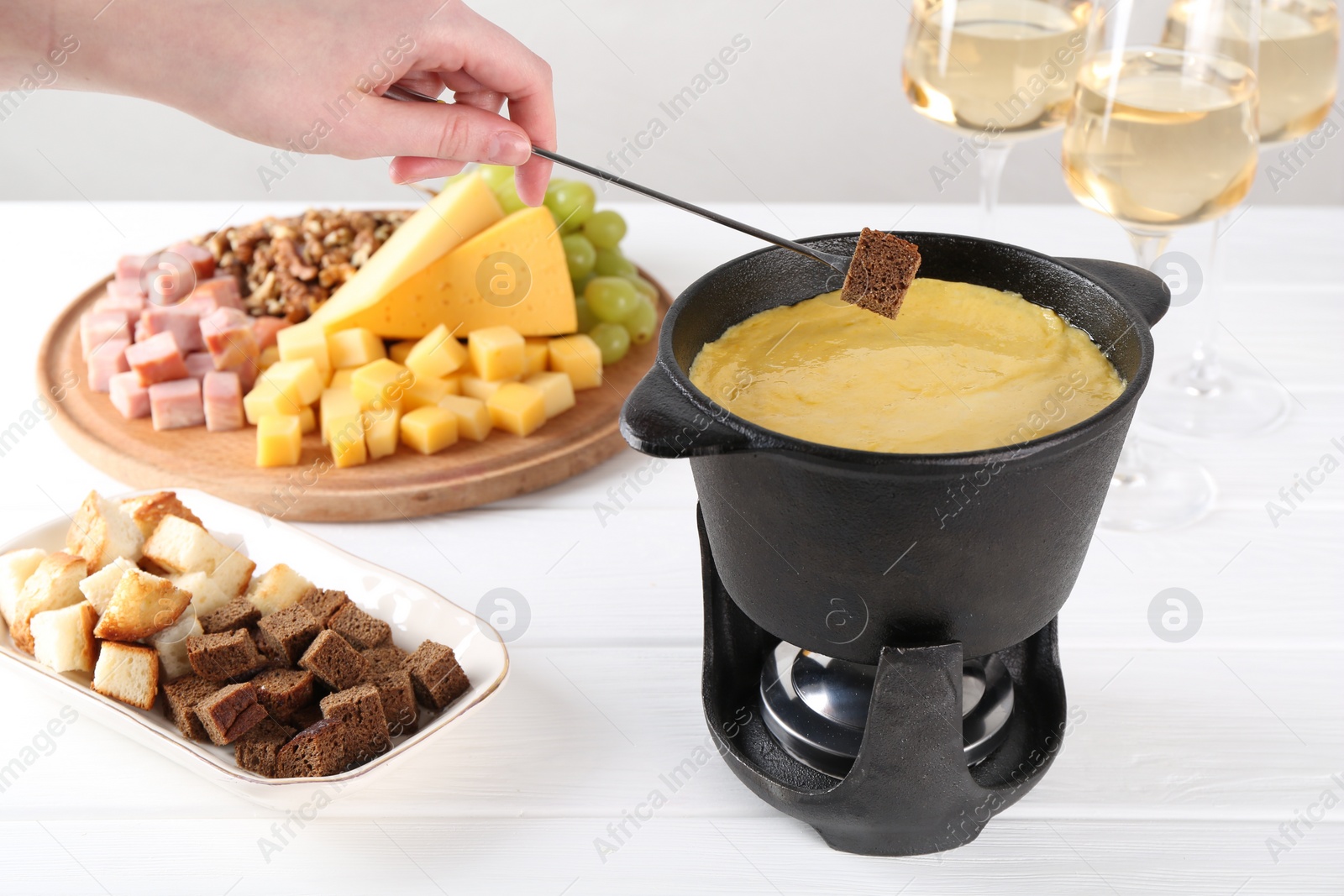 Photo of Woman dipping piece of bread into fondue pot with tasty melted cheese at white wooden table, closeup