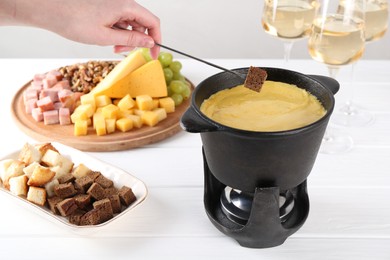 Photo of Woman dipping piece of bread into fondue pot with tasty melted cheese at white wooden table, closeup