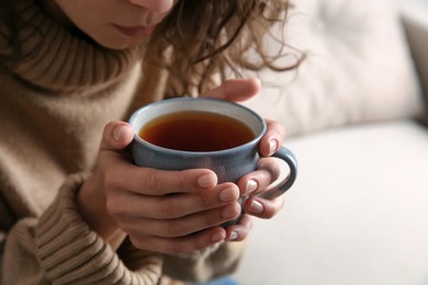 Photo of Woman with cup of hot tea indoors, closeup. Cozy home atmosphere