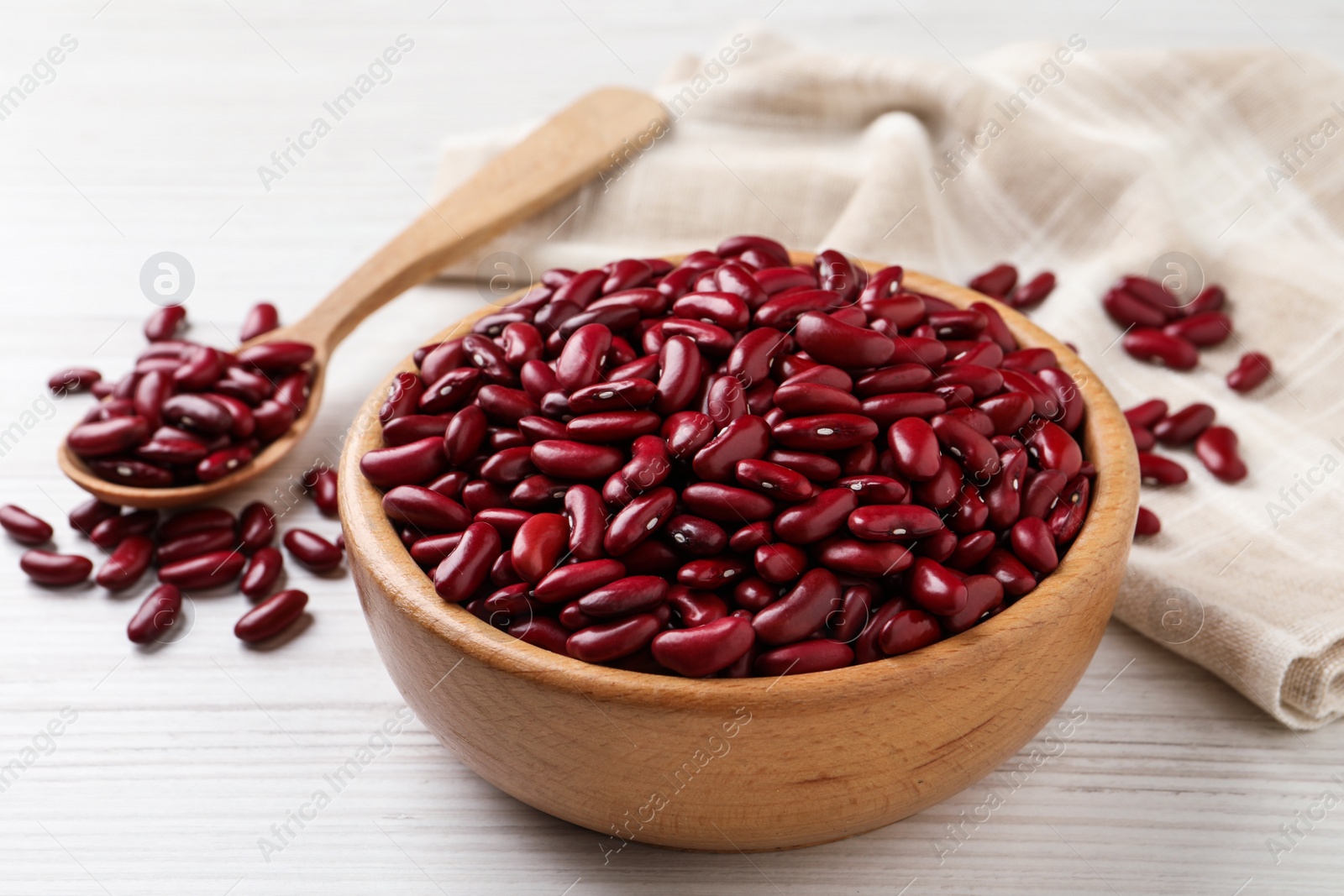 Photo of Raw red kidney beans with bowl and spoon on white wooden table