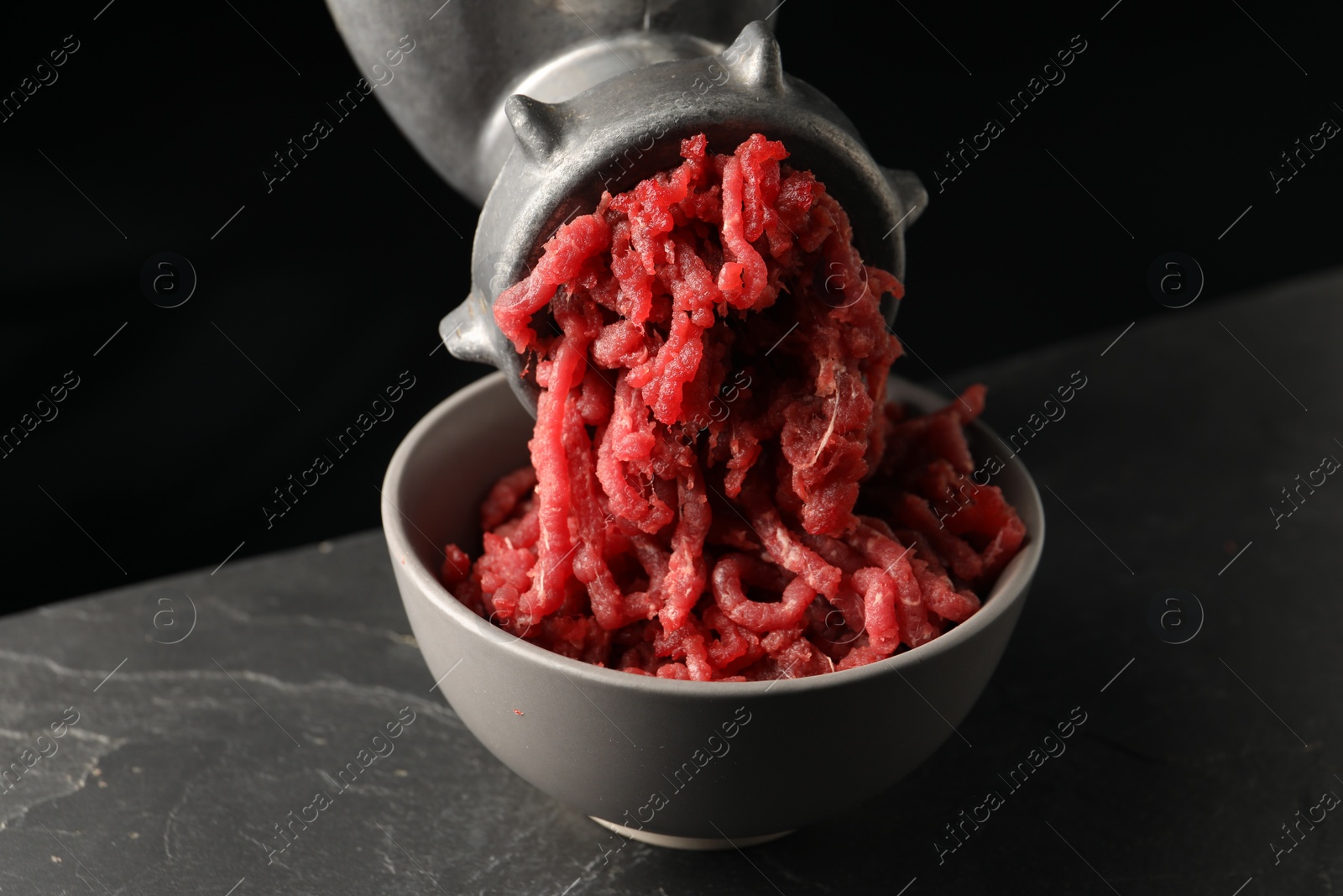 Photo of Metal meat grinder with beef mince on dark textured table against black background, closeup