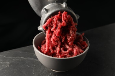 Metal meat grinder with beef mince on dark textured table against black background, closeup