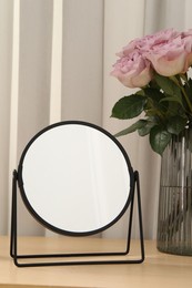 Photo of Mirror and vase with pink roses on wooden dressing table, closeup