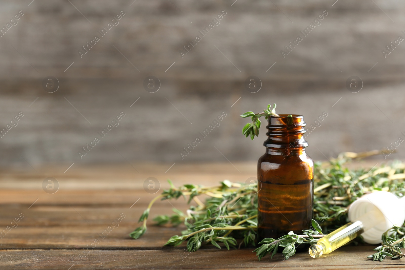 Photo of Bottle of essential oil with thyme on wooden table