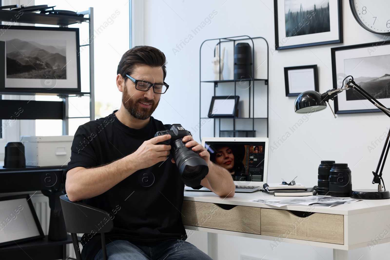 Photo of Professional photographer in glasses holding digital camera at table in office