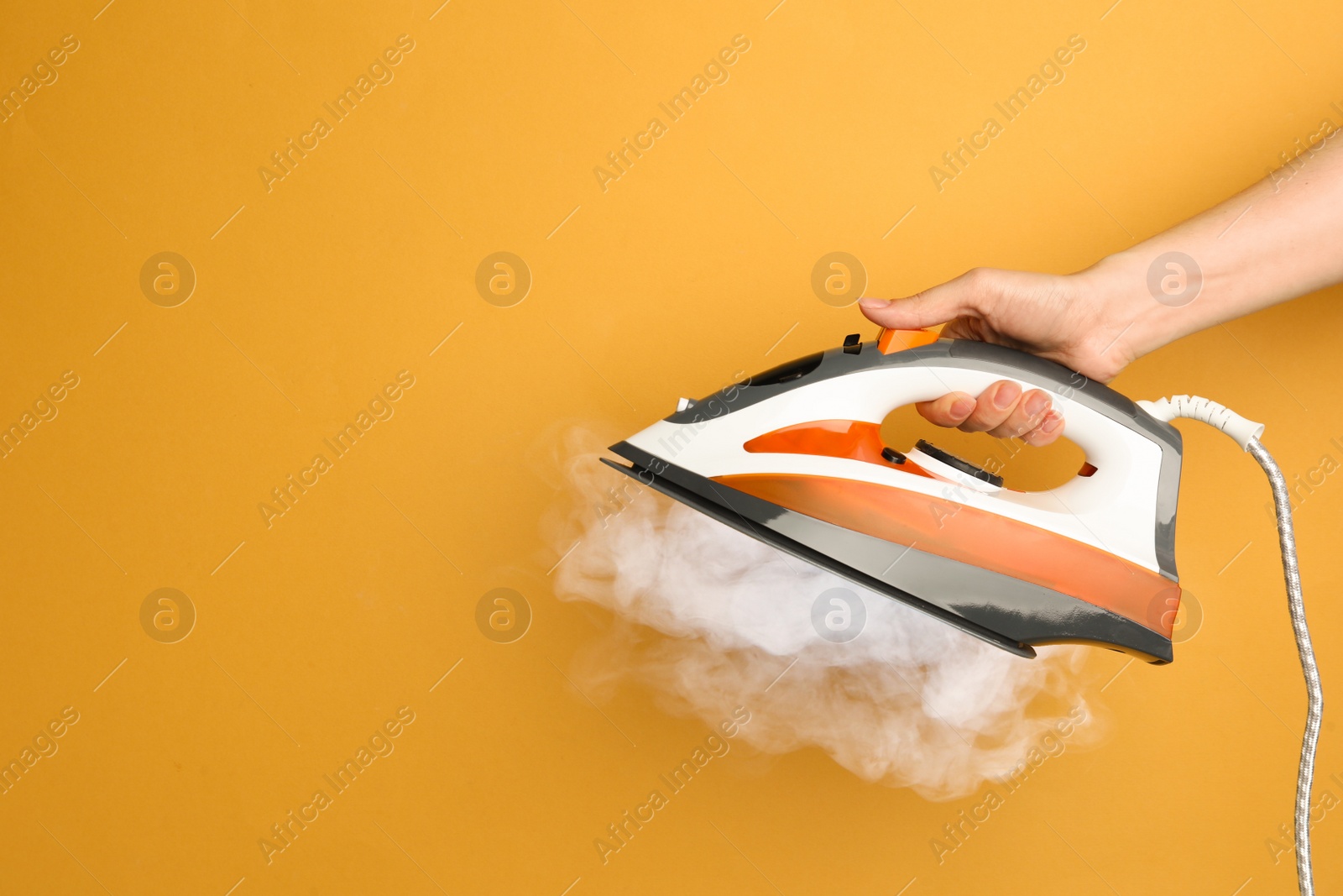 Image of Woman holding modern iron with steam on orange background, closeup. Space for text