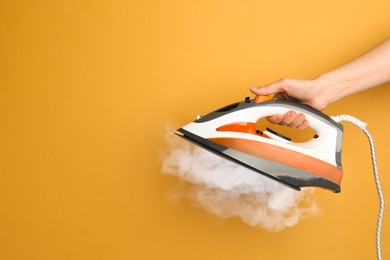 Image of Woman holding modern iron with steam on orange background, closeup. Space for text