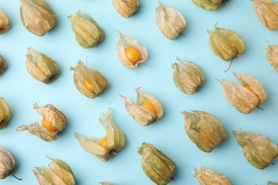 Photo of Ripe physalis fruits with calyxes on light blue background, flat lay