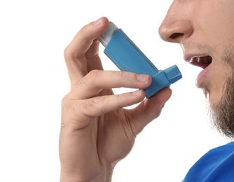 Young man using asthma inhaler on white background, closeup