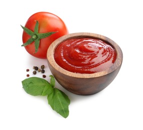 Photo of Tasty ketchup in wooden bowl, fresh tomatoes, peppercorns and basil isolated on white