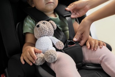 Photo of Mother fastening her daughter in child safety seat inside car, closeup