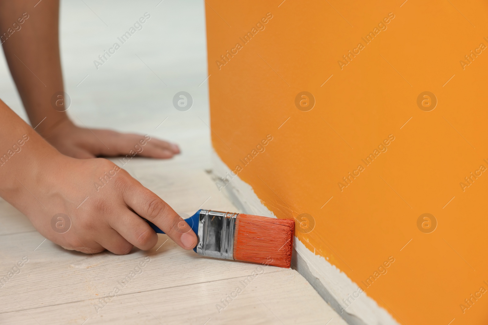 Photo of Worker using brush to paint wall with orange dye indoors, closeup