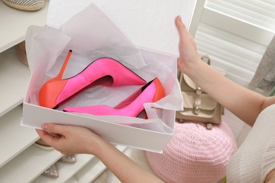 Photo of Woman holding box with high heeled shoes near rack indoors, closeup