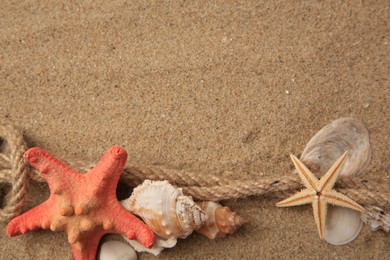 Beautiful sea stars, shells and rope on sand, flat lay. Space for text