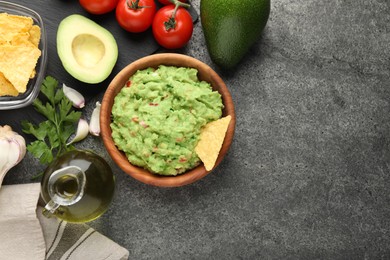 Photo of Delicious guacamole with nachos chips and ingredients on grey table, flat lay. Space for text