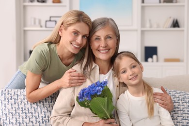 Photo of Three generations. Happy grandmother with beautiful cornflowers, her daughter and granddaughter at home