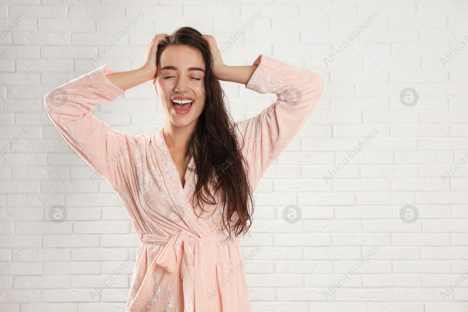 Photo of Young woman in bathrobe with wet hair near white brick wall. Space for text