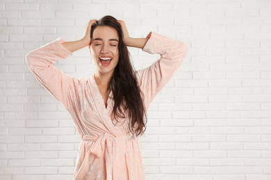 Young woman in bathrobe with wet hair near white brick wall. Space for text