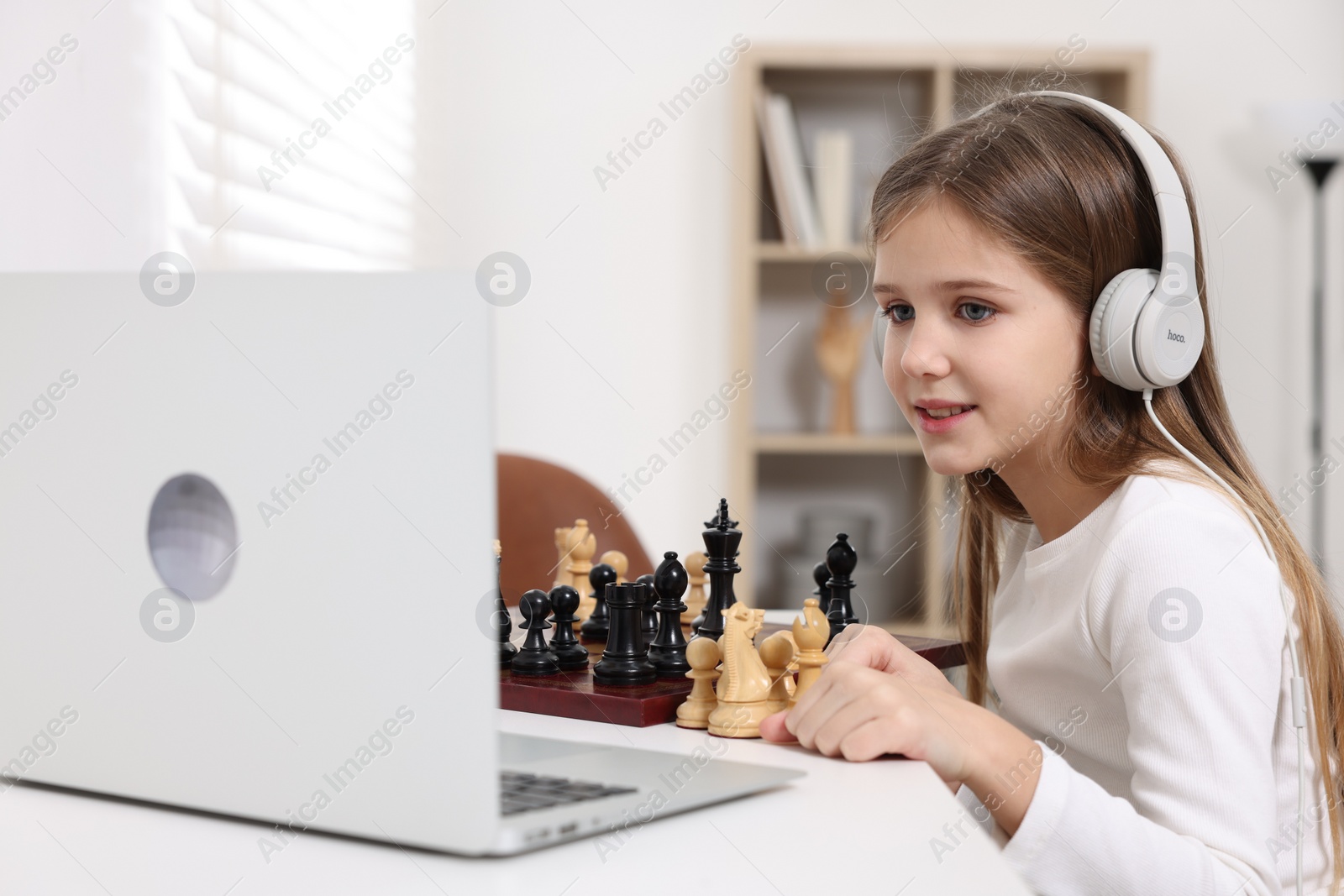 Photo of Cute girl learning to play chess with online tutor at home