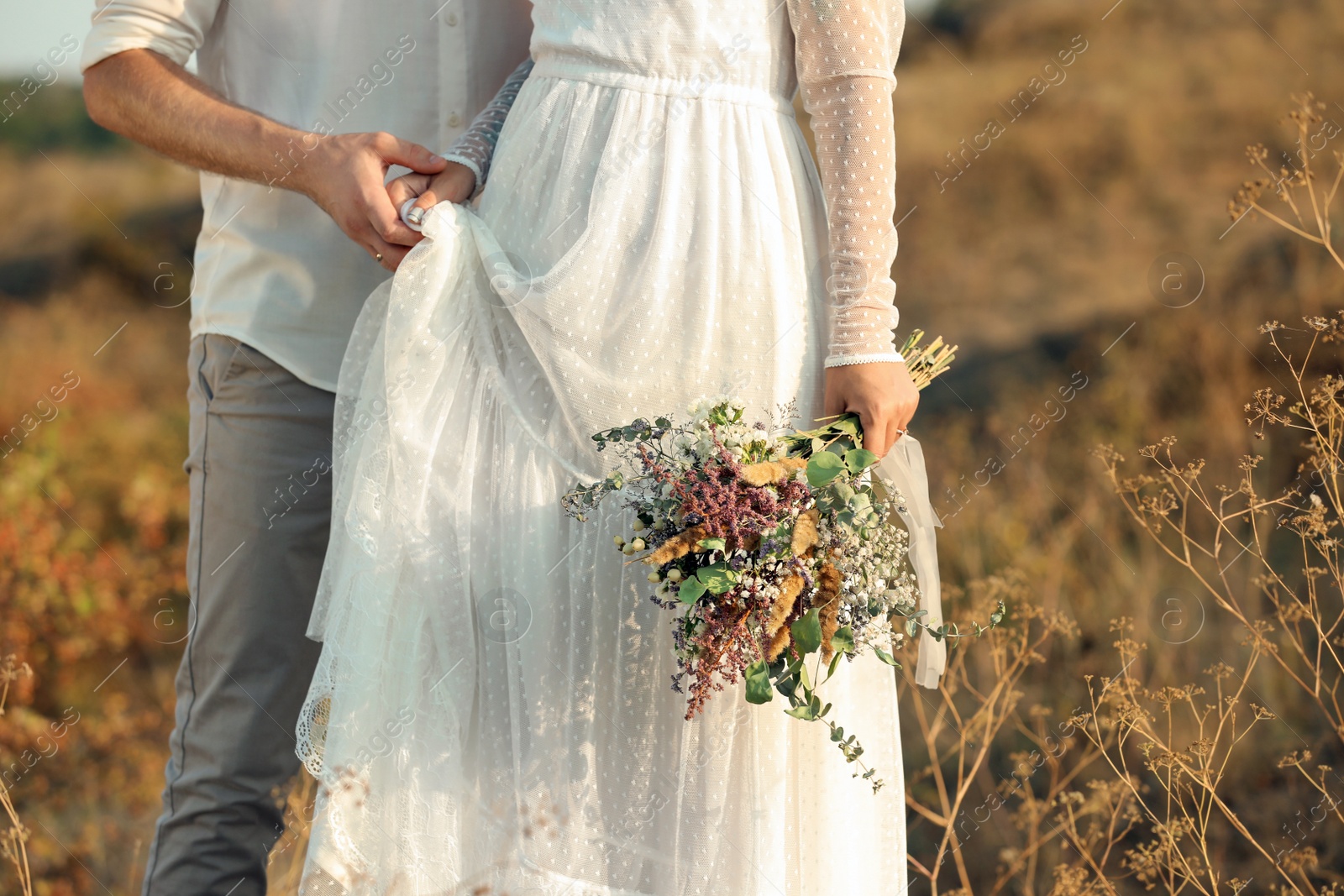 Photo of Happy newlyweds with beautiful field bouquet outdoors, closeup