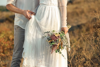 Photo of Happy newlyweds with beautiful field bouquet outdoors, closeup