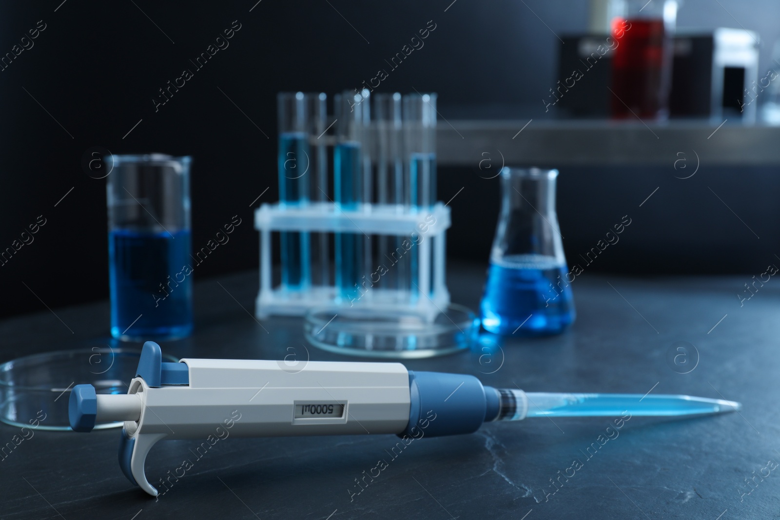 Photo of Laboratory analysis. Micropipette with liquid and different glassware on black table