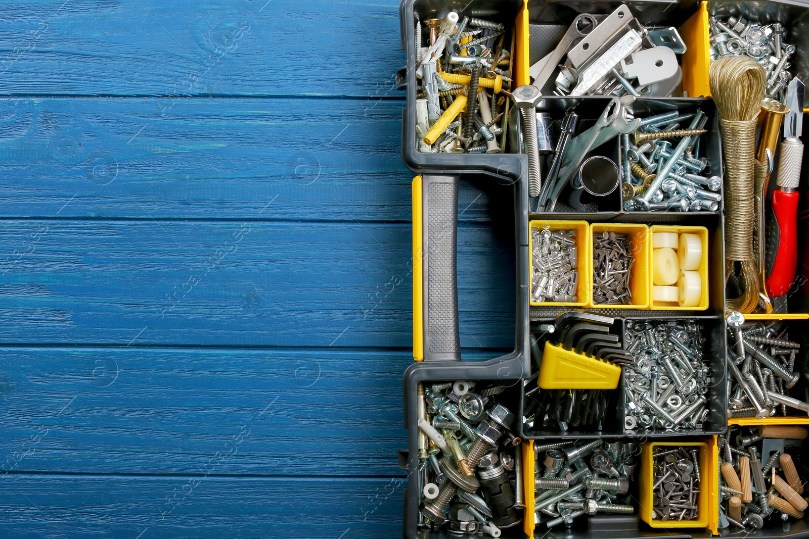 Photo of Plastic box with different furniture fittings and tools on blue wooden table, top view. Space for text