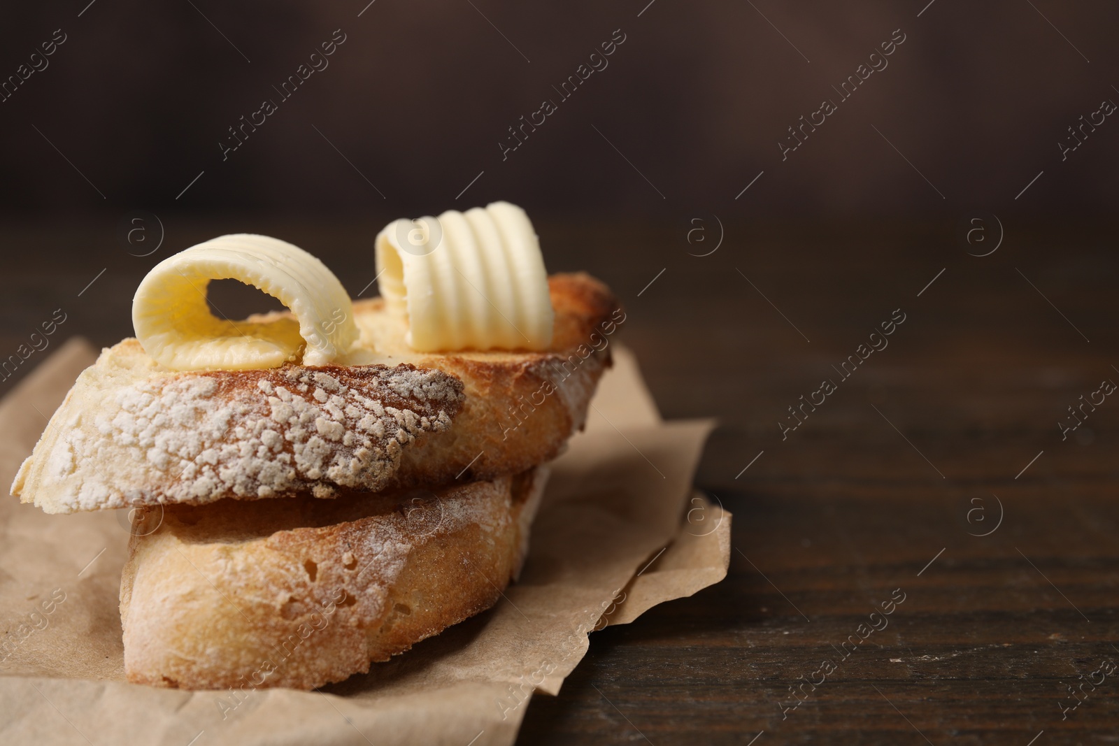 Photo of Tasty butter curls and slices of bread on wooden table, closeup. Space for text