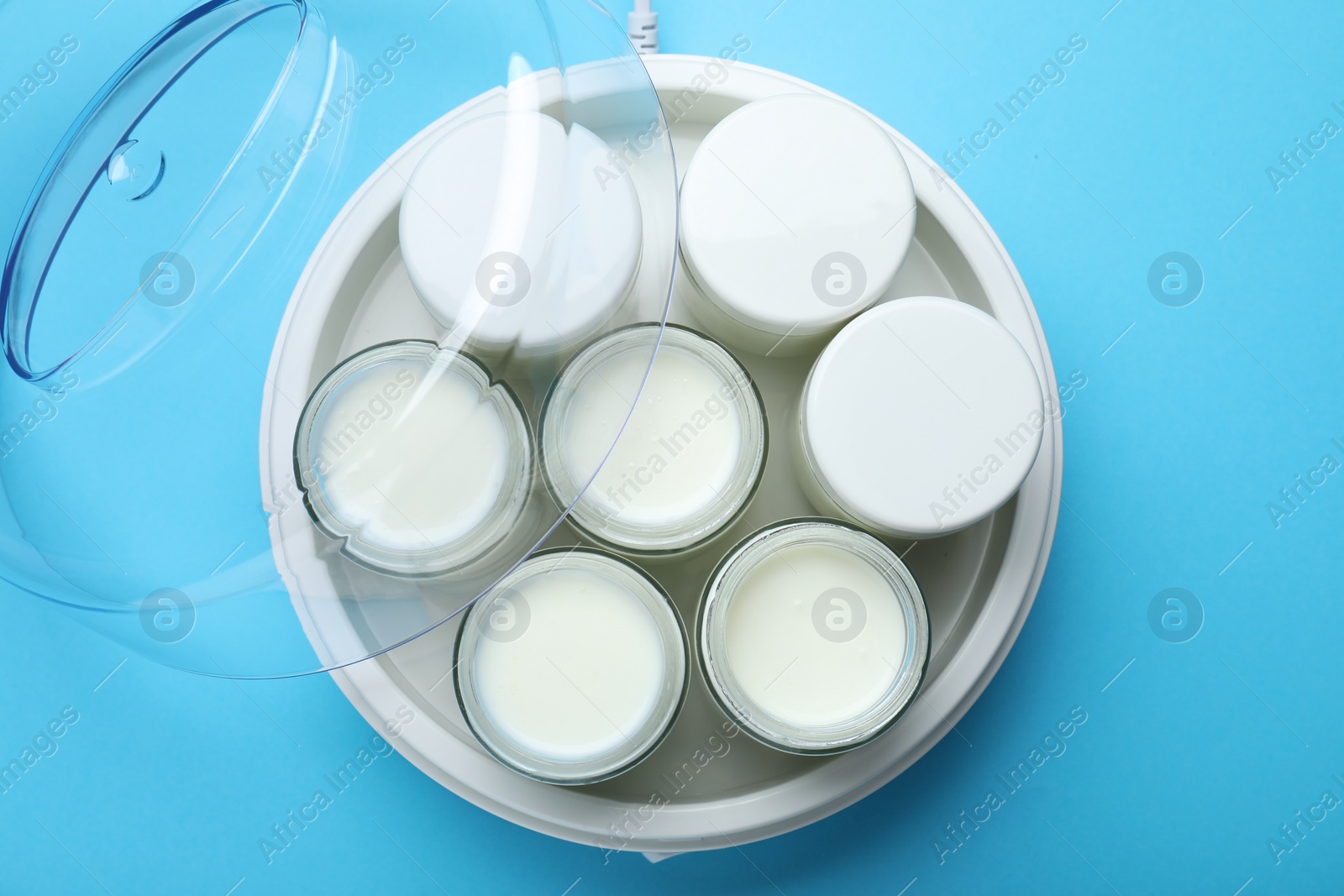 Photo of Modern yogurt maker with full jars on light blue background, top view