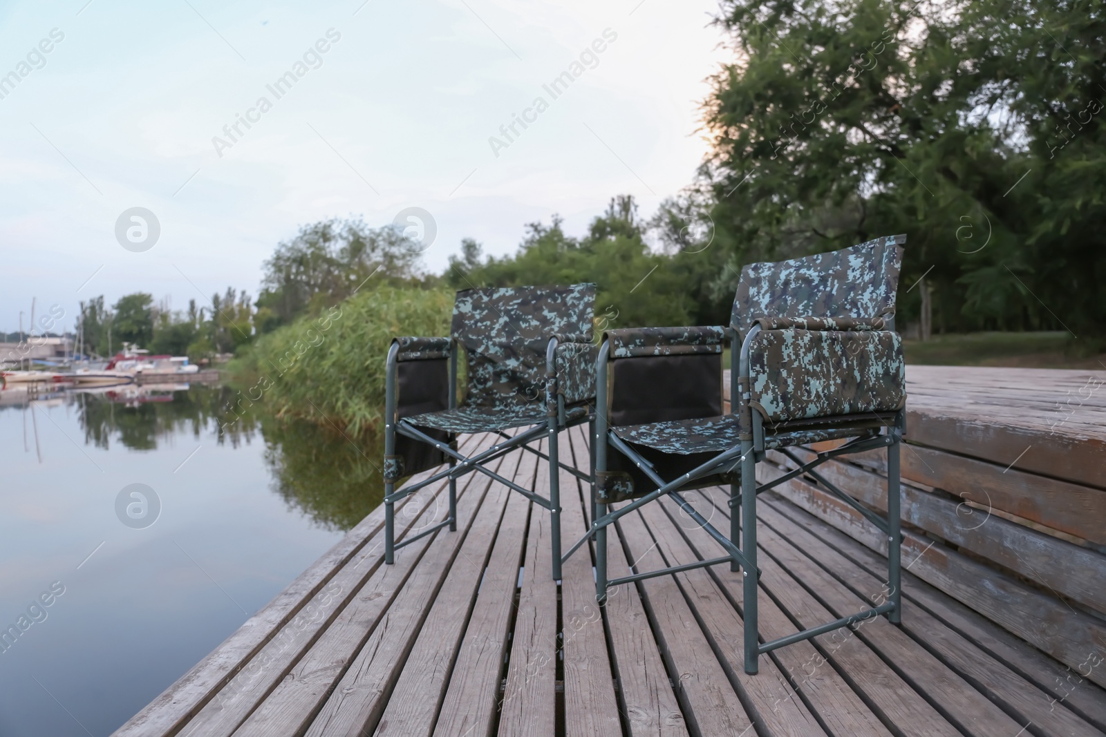 Photo of Camouflage fishing chairs on wooden pier near river