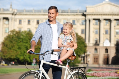 Happy father and his daughter with bicycle outdoors on sunny day