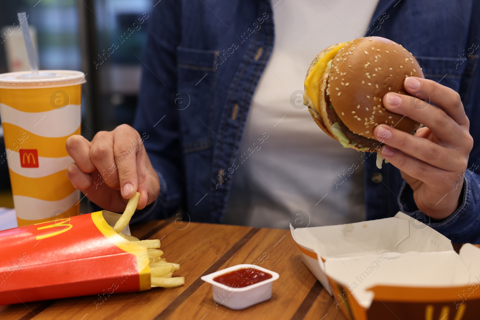 Photo of Lviv, Ukraine - October 9, 2023: Woman with McDonald's menu at wooden table in restaurant, closeup