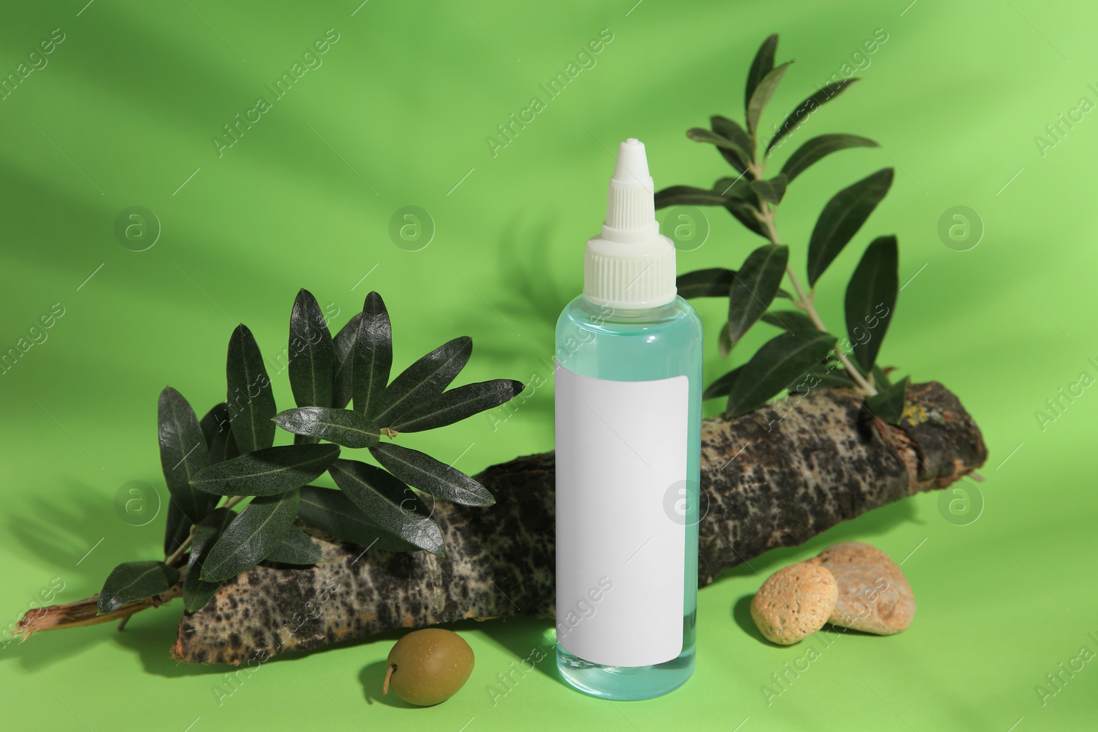 Photo of Bottle of cosmetic product, olives and leaves on light green background