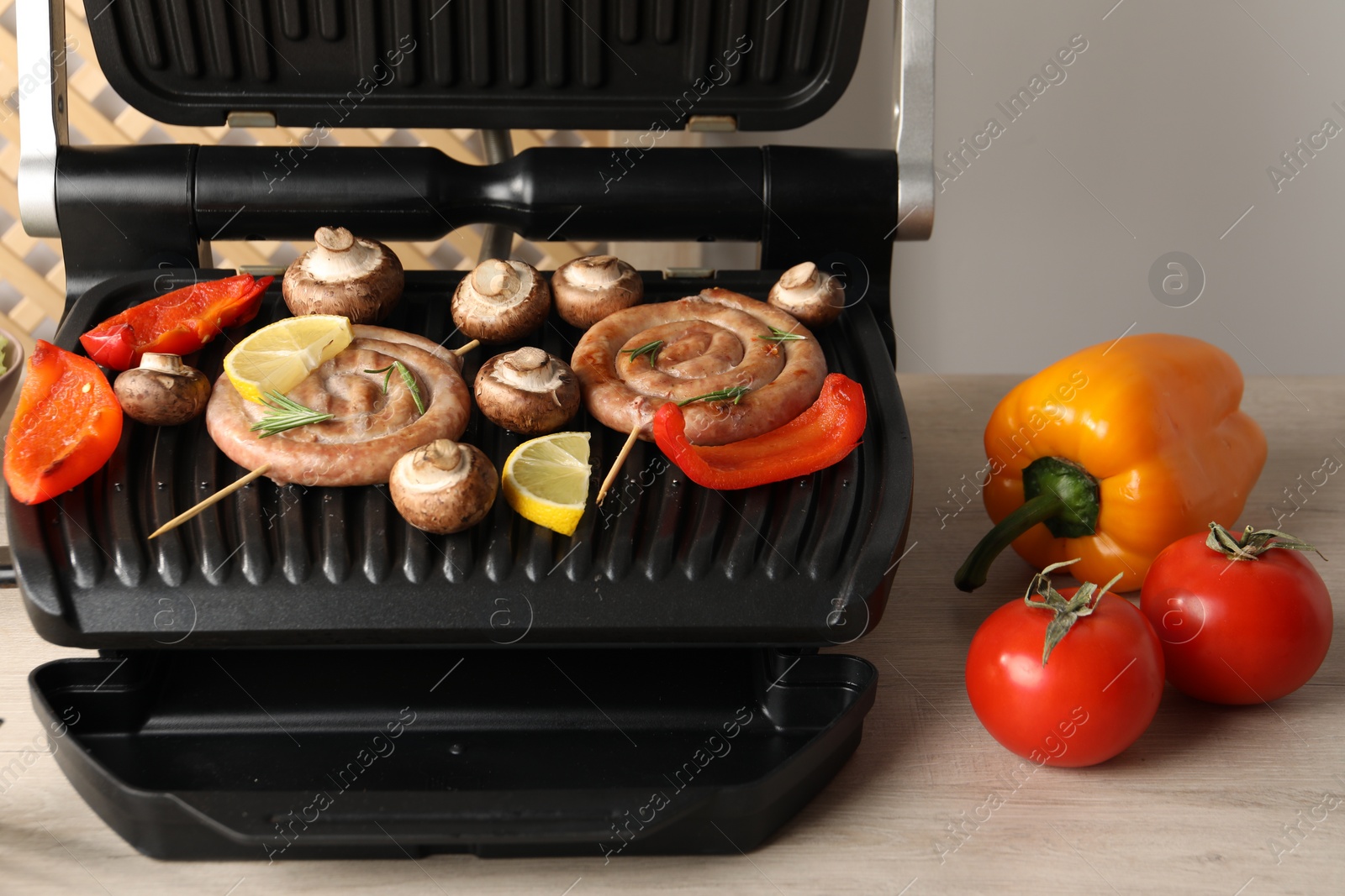 Photo of Electric grill with homemade sausages, bell peppers and mushrooms on wooden table