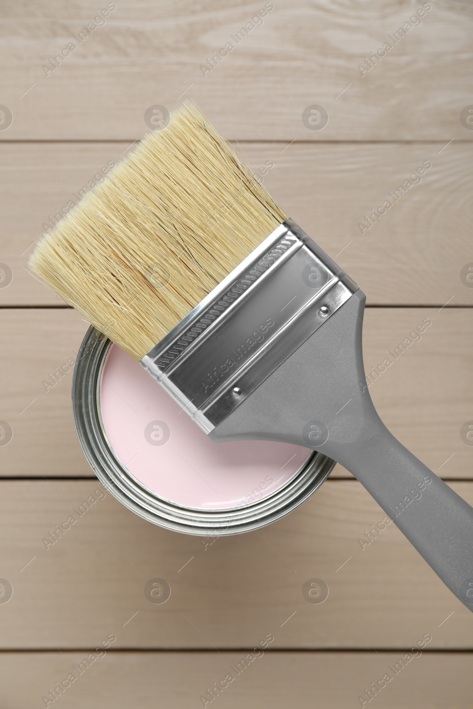 Photo of Can of pale pink paint with brush on wooden table, top view