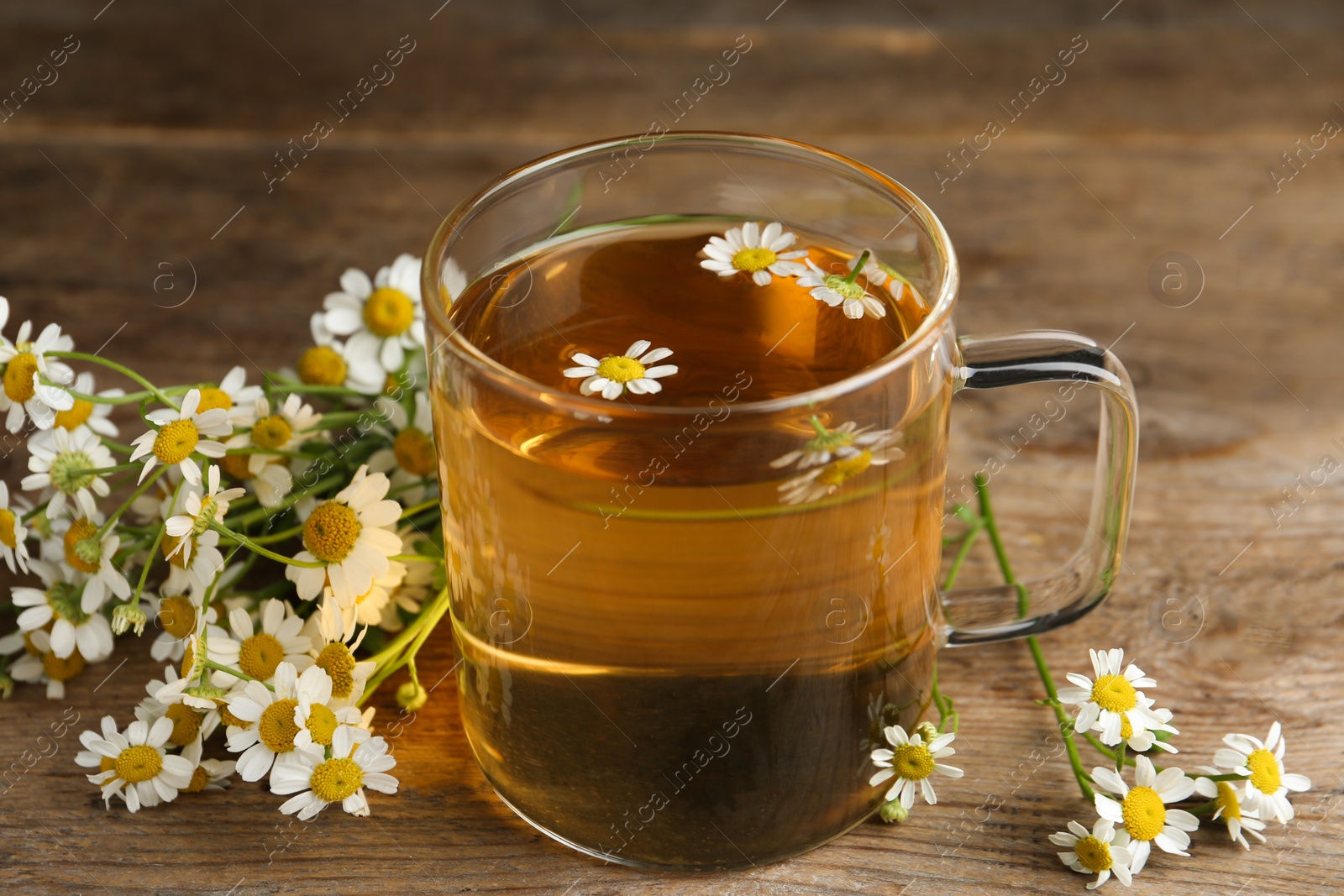 Photo of Cup of tea and chamomile flowers on wooden table