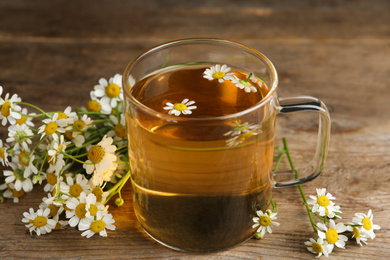 Cup of tea and chamomile flowers on wooden table