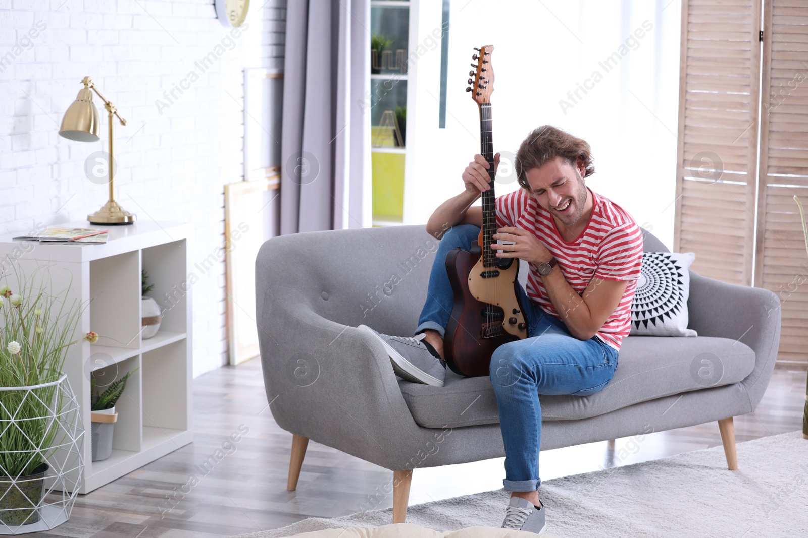 Photo of Young man playing electric guitar in living room. Space for text