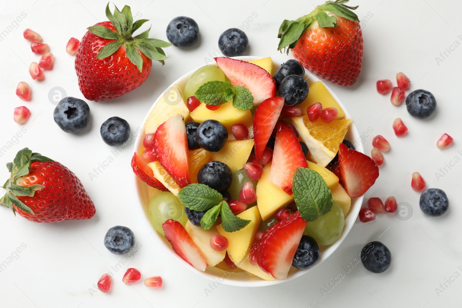 Photo of Tasty fruit salad in bowl and ingredients on white table, flat lay