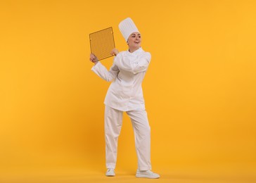Photo of Happy professional confectioner in uniform holding cooling rack on yellow background. Space for text