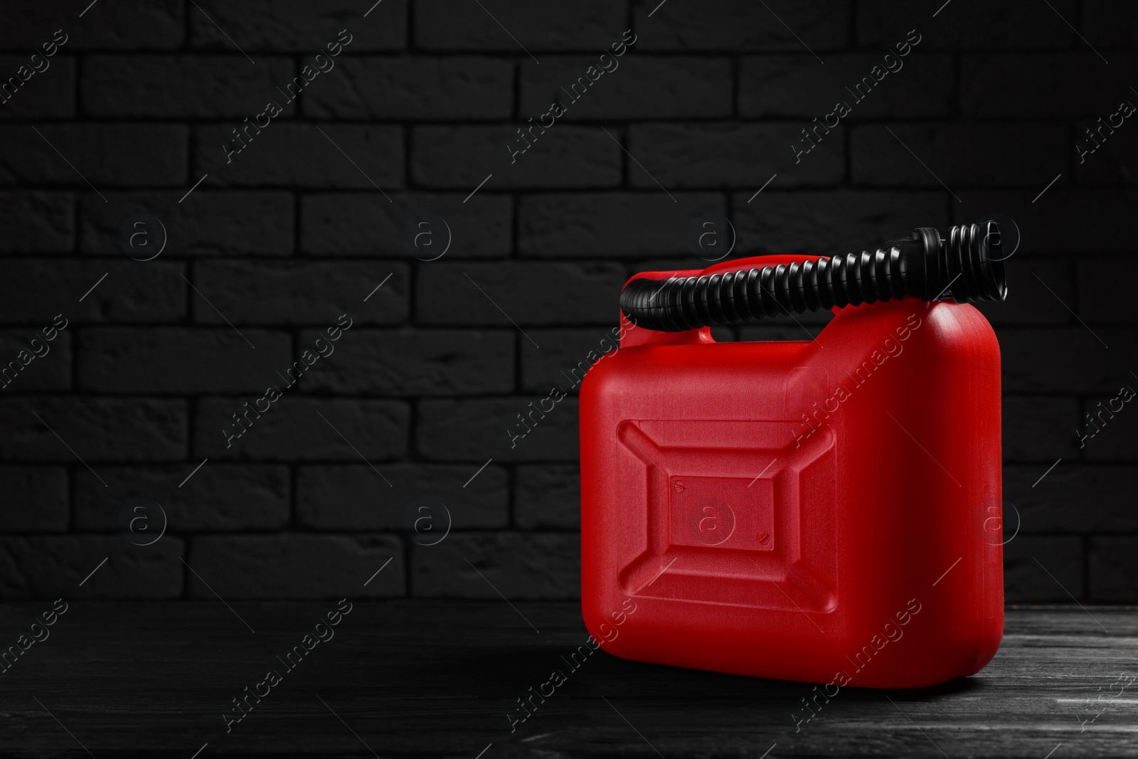 Photo of Red plastic canister on black wooden table against dark brick wall, space for text